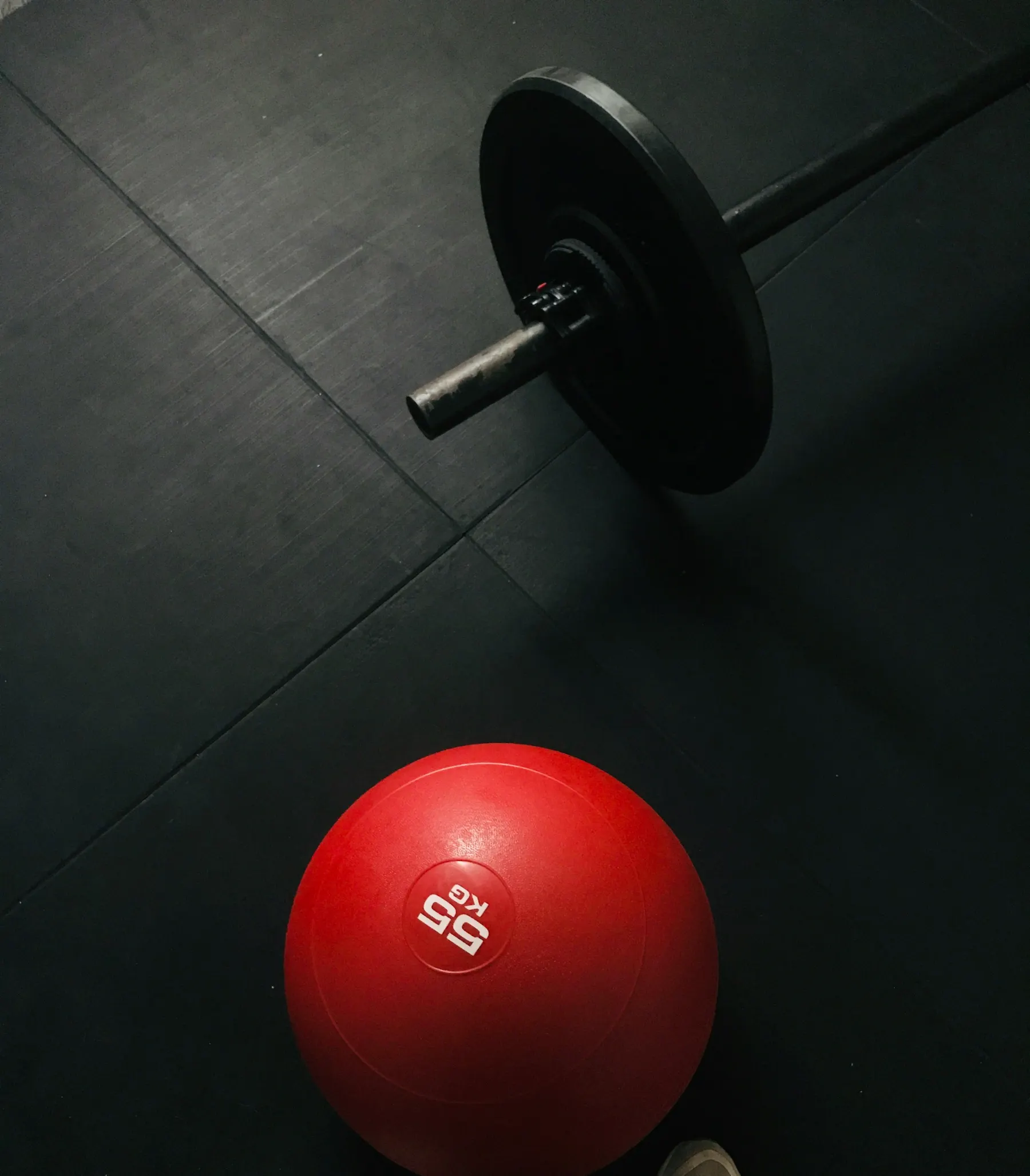 Barra olímpica con disco y balón medicinal rojo sobre el suelo de goma de la sala de entrenamiento